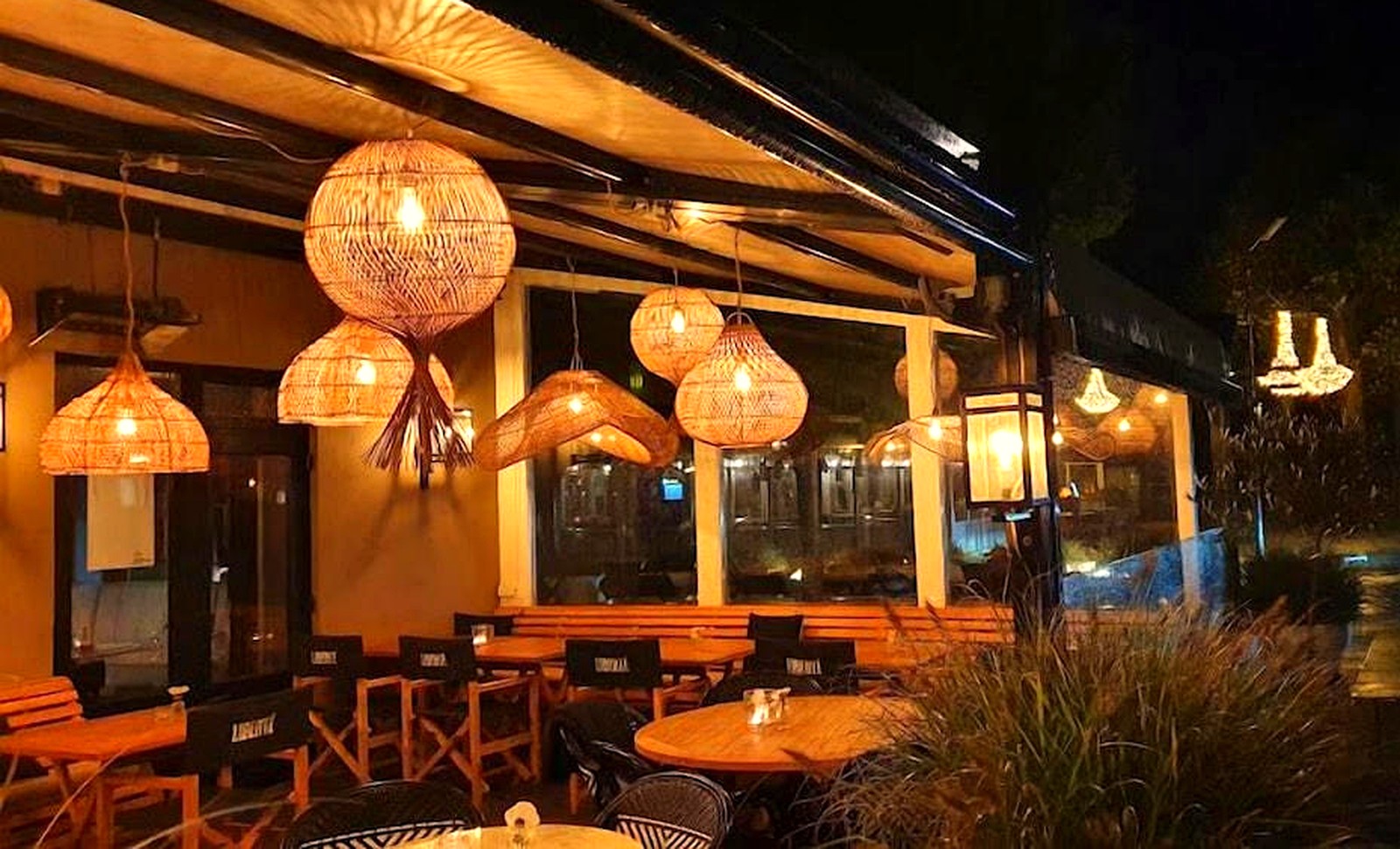 Terras van Liberté bij avond, met rotan hanglampen en houten tafels